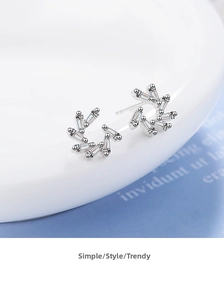 Detailed macro view of silver pin earrings with zircon crystals on white ceramic