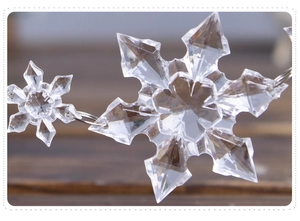 Macro shot of clear acrylic snowflake ornament with faceted crystal design on wood background