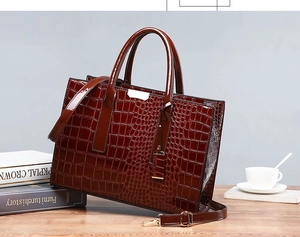 Detail of dark brown crocodile embossed leather handbag with glossy finish and gold buckle