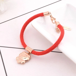 Detailed close-up of a red braided rope bracelet with a rose gold pig charm on white porcelain
