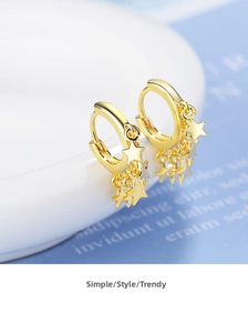 Detailed macro view of gold-plated star charm hoop earrings on a white porcelain edge