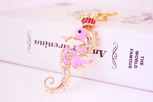 Macro detail of seahorse keychain with pink enamel, crystals, and a golden crown