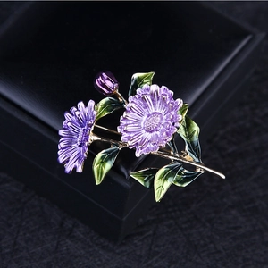 Detail of a purple enamel daisy flower brooch with gold alloy leaves on a black box