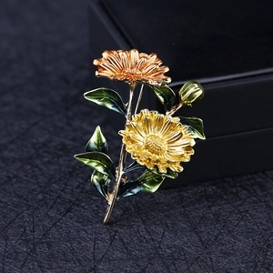 Macro shot of gold-plated daisy flower brooch with vibrant green enamel leaves