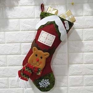 Festive red and green Christmas stocking with reindeer and snow motifs on white brick wall