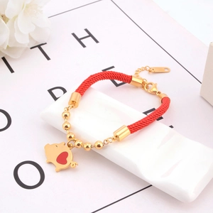 Detail of red braided bracelet featuring a golden pig charm and adjustable metal clasp