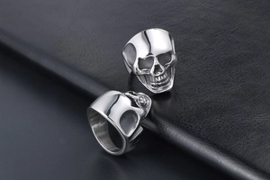 Detailed view of silver stainless steel skull rings displayed on black leather background