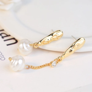 Detailed close-up of gold baroque pearl earrings with delicate chain and zircon stones