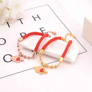 Detail of red rope bracelet with cute pig heart pendant and golden bead chain
