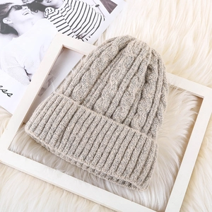 Detailed view of oatmeal cable knit beanie with thick mohair texture on white carpet