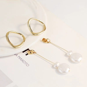 Detail view of long gold pearl earrings and geometric hoop earrings on a ceramic plate