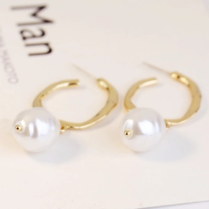 Detail of elegant gold C-shaped earrings featuring large lustrous white baroque pearls