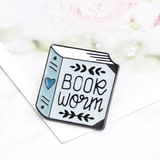Macro shot of a light blue and white enamel book pin featuring Book Worm text