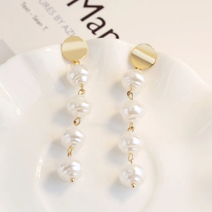Detailed macro of gold dangling earrings with white baroque pearls on white ceramic