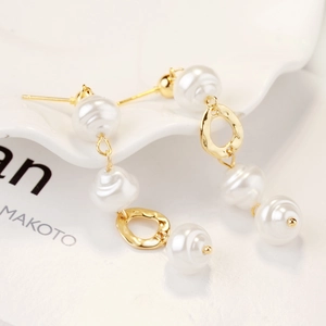 Close-up of gold baroque pearl drop earrings on a white decorative ceramic plate