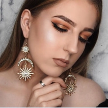 Close-up of dangling gold sun and crescent moon earrings with rhinestones on model