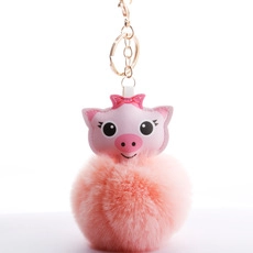 Detailed view of a pink plush pompom keychain with a leather pig charm and golden clasp