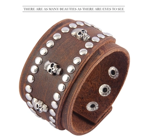 Close-up of brown leather punk bracelet featuring silver skull charms and metal rivets