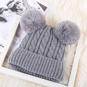 Detailed knit texture of a grey winter beanie featuring double faux fur pom-poms on top