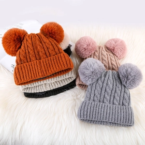 Detailed close-up of colorful winter knit hats with double faux fur pom-poms on plush rug