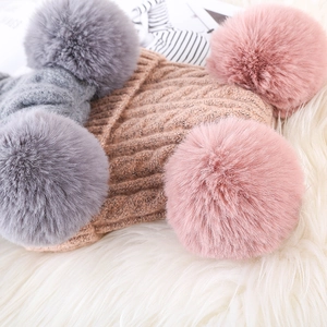 Detailed cable knit texture and fluffy faux fur pom-poms on grey and pink winter beanies