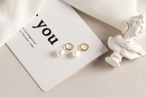 Detail of gold hoops with baroque pearls on silk fabric beside a classical white bust