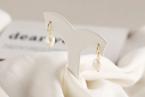 Detail of baroque pearl earrings with gold accents and silk fabric background