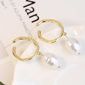 Close-up of golden irregular lava texture earrings with dangling baroque pearls