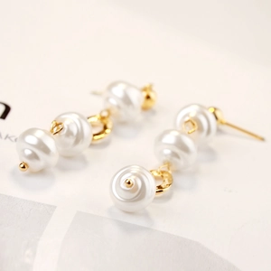 Macro detail of triple-layered baroque pearl earrings with golden metal findings