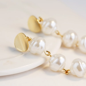 Macro shot of long baroque pearl earrings with textured white pearls and gold round studs