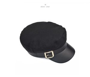 Detail of black wool newsboy cap featuring matte leather brim and golden metal buckle