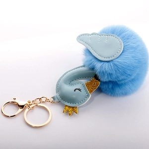 Macro detail of blue swan pompom keychain with golden crown and leather wings