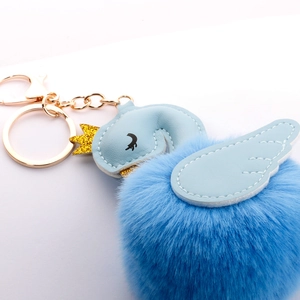 Detail of light blue swan faux fur keychain with gold crown and leather wing texture