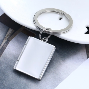 Polished silver book-shaped pendant keychain on white ceramic plate detail view