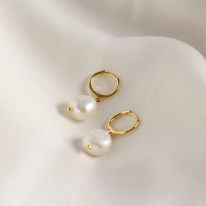 Macro view of gold hoop earrings with white freshwater pearls on silk background