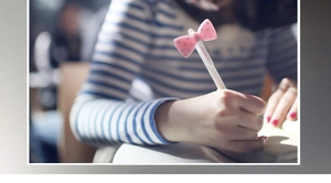 Detailed view of creative white pen with pink polka dot bow decoration held by hand