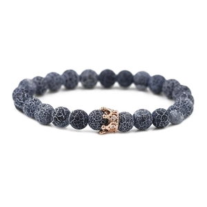 Macro detail of bead bracelet featuring black weathered stone and rose gold crown charm