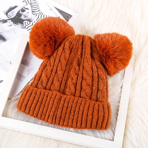 Cozy orange cable knit beanie with two large faux fur pom-poms for winter warmth