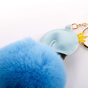 Close-up of soft blue faux fur pompom keychain with crown and gold-tone metal hardware