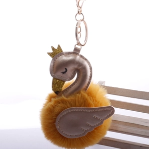 Detail of yellow fur ball swan keychain with golden crown on a mini white bench