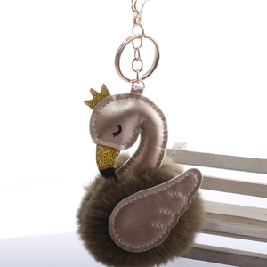 Detail of swan faux fur pompom keychain with golden crown and leather wings on white background