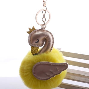Detail of yellow swan pompom keychain featuring a glitter crown and metallic wings