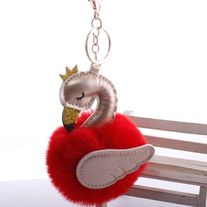 Close-up of red swan pom-pom keychain with golden crown and wings on white bench