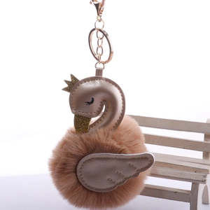 Swan faux fur pom pom keychain with gold leather crown and wings on a white chair