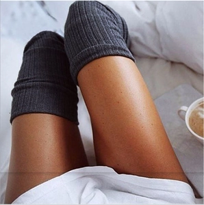 Detail of dark grey knitted thigh-high yoga socks with ribbed texture on a cozy bed