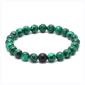 Macro detail of natural malachite beads and a single black matte stone on a stretch bracelet