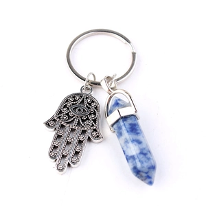 Detailed shot of Hamsa hand charm and hexagonal blue stone pendant on silver keychain