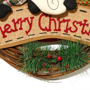 Detalle de letras de fieltro Merry Christmas y agujas de pino en corona de ratán rústica