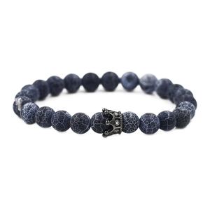 Macro detail of dark blue weathered stone beads and black gold crown charm on bracelet