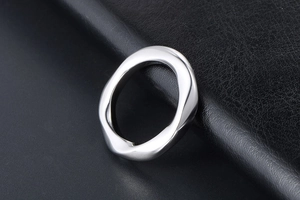 Gros plan d'une bague argentée ondulée sur un fond de cuir noir texturé